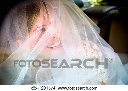 Picture - Bride in full wedding veil looking back and smiling. Fotosearch