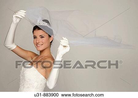 Stock Image - Bride in her 20s discovers herself from under her veil. Fotosearch
