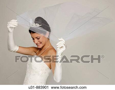 Stock Image - Bride in her 20s discovers herself from under her veil. Fotosearch