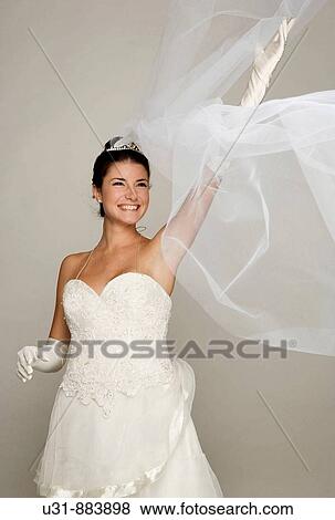 Stock Photo - Bride in her 20s discovers herself from under her veil. Fotosearch