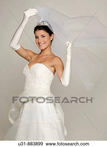Stock Photo - Bride in her 20s discovers herself from under her veil. Fotosearch