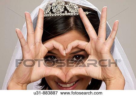 Stock Photo - Bride in her 20s draws a heart with her hands at the camera. Fotosearch