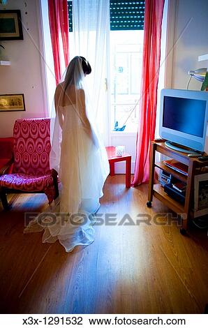 Stock Image - Bride in wedding dress looking out the window door. Fotosearch