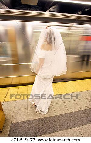 Stock Photo - Bride in wedding dress on subway station platform with back to camera as train goes by in motion. Fotosearch