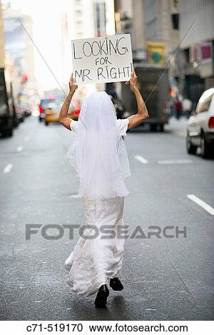 Bride in wedding dress running Downtreet with back to camera holding a sign overhead reading? Looking for Mr. Right? View Large Photo Image Stock Image - Bride in wedding dress running Downtreet with back to camera holding a sign overhead reading? Looking for Mr. Right?. Fotosearch