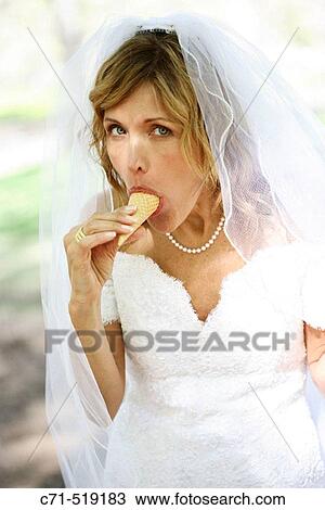 Stock Image - bride in wedding dress with ice cream cone in her mouth. Fotosearch