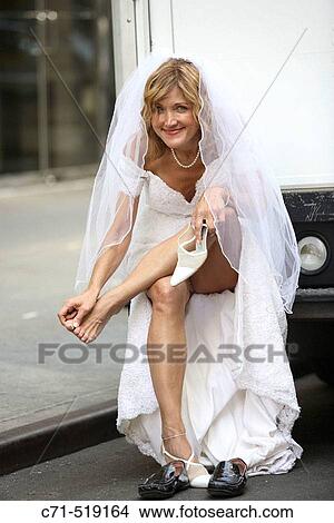Picture - Bride sitting on bumber of truck rubbing her tired feet. Fotosearch
