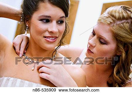 Stock Photo - Bridesmaid helping bride with necklace. Fotosearch