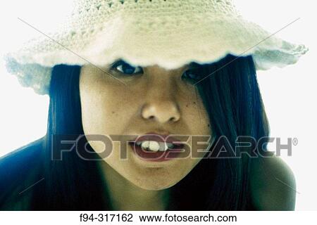 Stock Image - Brightly backlit portrait of young woman with hat. Fotosearch