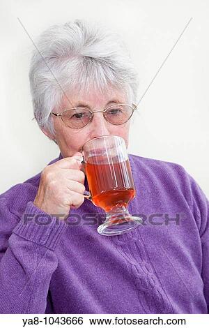 Stock Photograph - Britain UK Europe Senior woman drinking red fruit tea in a glass mug MR 09/06. Fotosearch