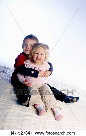 Stock Photo - brother, age 4 and sister, age 3, sitting in a row on the floor, studio, smiling and hugging. Fotosearch