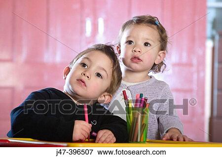 Stock Photo - Brother and sister 3 and 1, standing drawing at a desk, looking off camera. Fotosearch