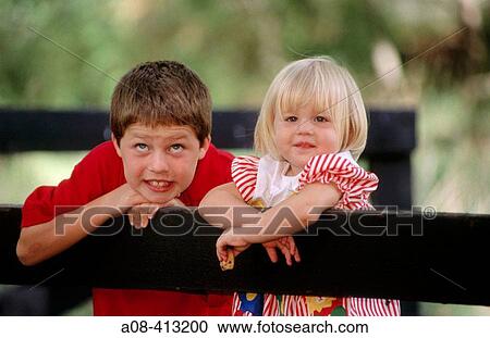Stock Image - Brother and sister lean on split rail fence. USA.. Fotosearch