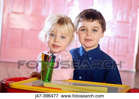 Stock Photo - Brother and sister sitting at a desk smiling into camera. Fotosearch