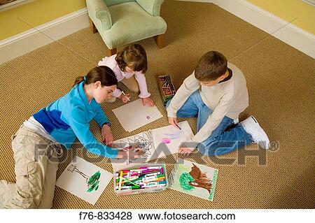 Stock Photo - Brother and sisters sitting on rug and drawing in sketchbooks with colored markers and crayons. Fotosearch