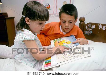 Brother helps small sister read a book at bedtime View Large Photo Image Stock Image - Brother helps small sister read a book at bedtime. Fotosearch