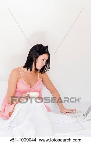 Bruentte woman enjoying breakfast sitting on the bed with laptop View Large Photo Image Picture - Bruentte woman enjoying breakfast sitting on the bed with laptop. Fotosearch
