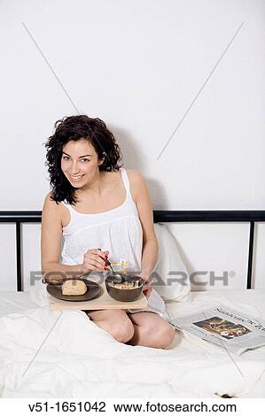 Stock Image - Brunette beautiful woman having breakfast in bed. Fotosearch