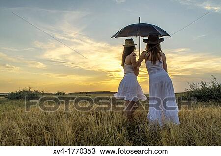 Brunette couple relaxing in the countryside look at horizont with umbrella View Large Photo Image Stock Image - Brunette couple relaxing in the countryside look at horizont with umbrella. Fotosearch
