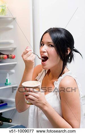 Brunette woman enjoying an ice cream at night in the kitchen beside the fridge View Large Photo Image Stock Photo - Brunette woman enjoying an ice cream at night in the kitchen beside the fridge. Fotosearch
