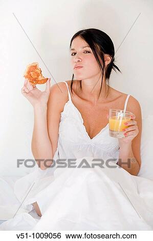 Stock Photograph - Brunette woman enjoying breakfast in bed. Fotosearch
