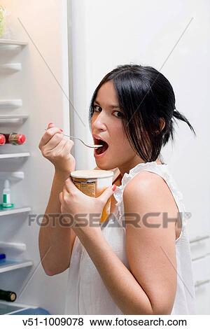 Brunette woman enjoying ice cream in the kitchen beside the fridge View Large Photo Image Stock Photo - Brunette woman enjoying ice cream in the kitchen beside the fridge. Fotosearch