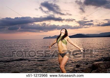 Stock Photograph - Brunette woman in bikini by the sea at sunset. Fotosearch