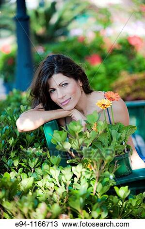 Brunette woman in summer dress in garden setting sitting on a bench grinning to the camera. View Large Photo Image Stock Image - Brunette woman in summer dress in garden setting sitting on a bench grinning to the camera.. Fotosearch