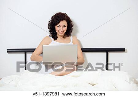 Brunette woman with laptop in bed View Large Photo Image Stock Image - Brunette woman with laptop in bed. Fotosearch