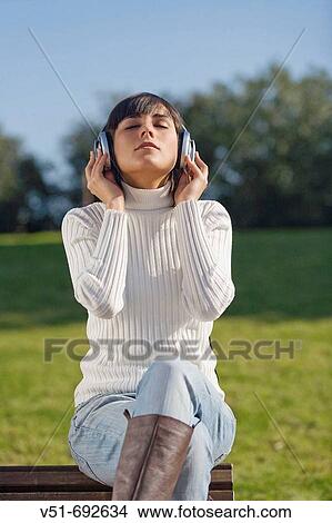 Brunette young woman enjoying music in the park View Large Photo Image Picture - Brunette young woman enjoying music in the park. Fotosearch