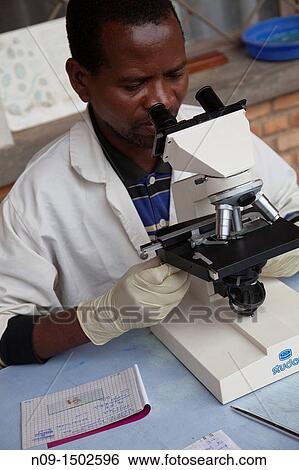 Stock Photograph - Burundi, nurse looks into the microscope. Fotosearch