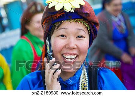 Stock Image - Buryatian woman in traditional dress talks on a mobile phone in the "Old Believers'" village of Turbagatai, near Ulan Ude, Buryatia, Siberia, Russia.. Fotosearch
