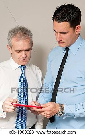 Stock Photo - Business colleagues, one young and one older, discuss work using tablet computer. Fotosearch