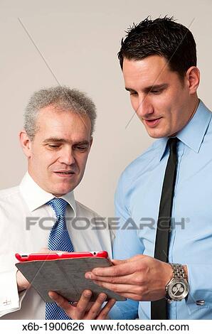 Business colleagues, one young and one older, discuss work using tablet computer View Large Photo Image Stock Photograph - Business colleagues, one young and one older, discuss work using tablet computer. Fotosearch