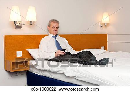 Business man sitting on hotel bed checking his phone for messages View Large Photo Image Stock Image - Business man sitting on hotel bed checking his phone for messages. Fotosearch