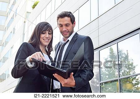Businessman and businesswoman look over paperwork while standing outside. View Large Photo Image Stock Image - Businessman and businesswoman look over paperwork while standing outside.. Fotosearch