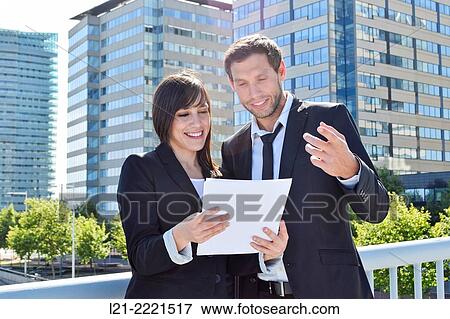 Businessman and businesswoman look over paperwork while standing outside. View Large Photo Image Stock Photo - Businessman and businesswoman look over paperwork while standing outside.. Fotosearch