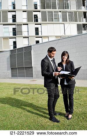 Businessman and businesswoman look over paperwork while standing outside. View Large Photo Image Stock Photo - Businessman and businesswoman look over paperwork while standing outside.. Fotosearch