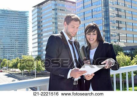 Businessman and businesswoman look over paperwork while standing outside. View Large Photo Image Stock Photograph - Businessman and businesswoman look over paperwork while standing outside.. Fotosearch