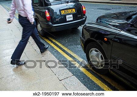 Businessman crossing the street between to Black Cab in Canary Wharf, London, UK View Large Photo Image Stock Photo - Businessman crossing the street between to Black Cab in Canary Wharf, London, UK. Fotosearch