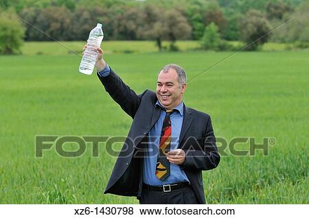 Stock Photo - businessman drink water at green field. Fotosearch