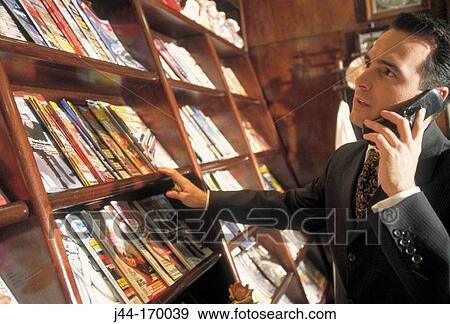 Stock Photo - Businessman in a bookstore talking on cellular phone. Fotosearch