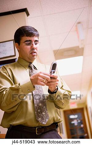 Businessman looking at cellular phone in an office View Large Photo Image Stock Image - Businessman looking at cellular phone in an office. Fotosearch