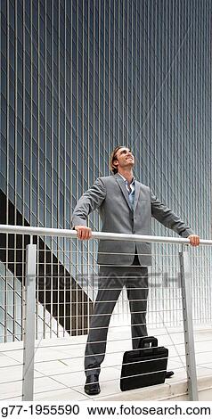 Stock Image - Businessman looking up under high rise building. New York. Usa.. Fotosearch