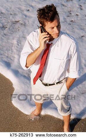 Stock Image - Businessman on cell phone at beach. Fotosearch