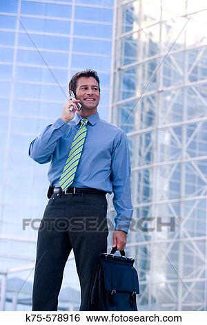 Businessman on cell phone by office building View Large Photo Image Stock Photograph - Businessman on cell phone by office building. Fotosearch