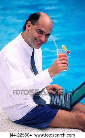 Picture - Businessman sitting on pool edge with drink working with laptop computer. Fotosearch