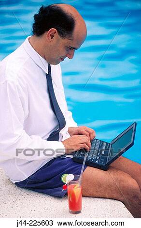 Businessman sitting on pool edge with drink working with laptop computer View Large Photo Image Stock Image - Businessman sitting on pool edge with drink working with laptop computer. Fotosearch