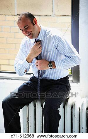 Businessman sitting on radiator fixing tie View Large Photo Image Stock Photo - Businessman sitting on radiator fixing tie. Fotosearch