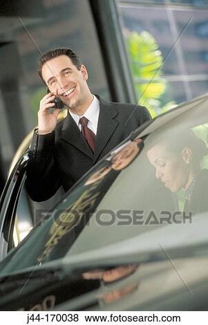 Businessman talking on a cellular phone by a car outdoors View Large Photo Image Stock Photo - Businessman talking on a cellular phone by a car outdoors. Fotosearch